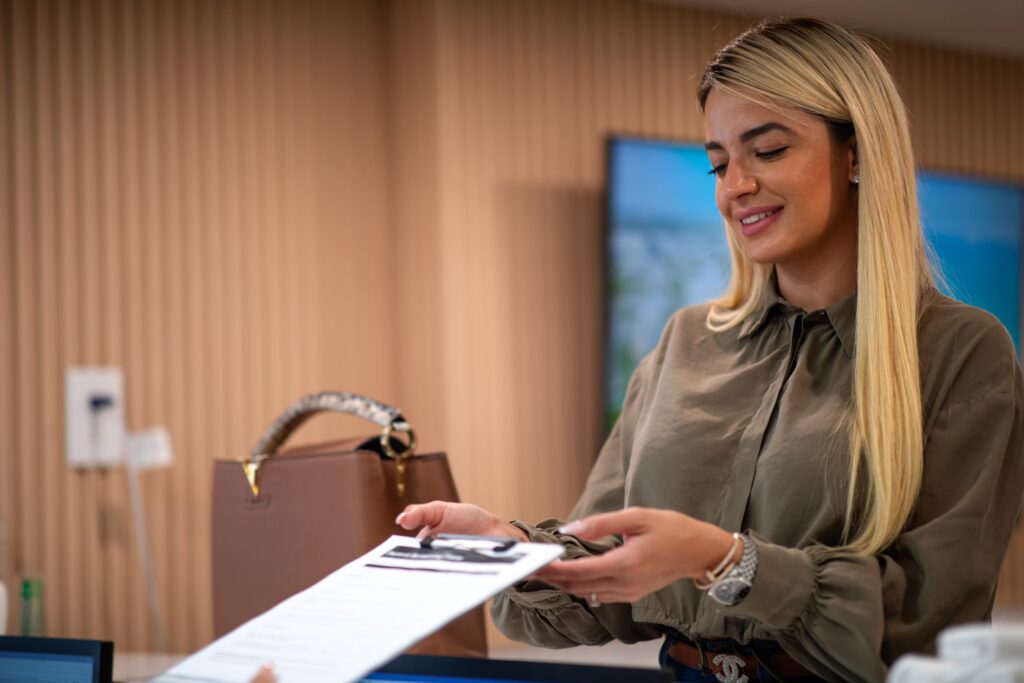 Smiling woman hands a document to someone in an office setting.